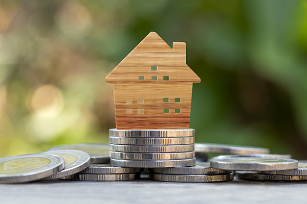 Wooden house model on coin pile and blurred green nature backgro